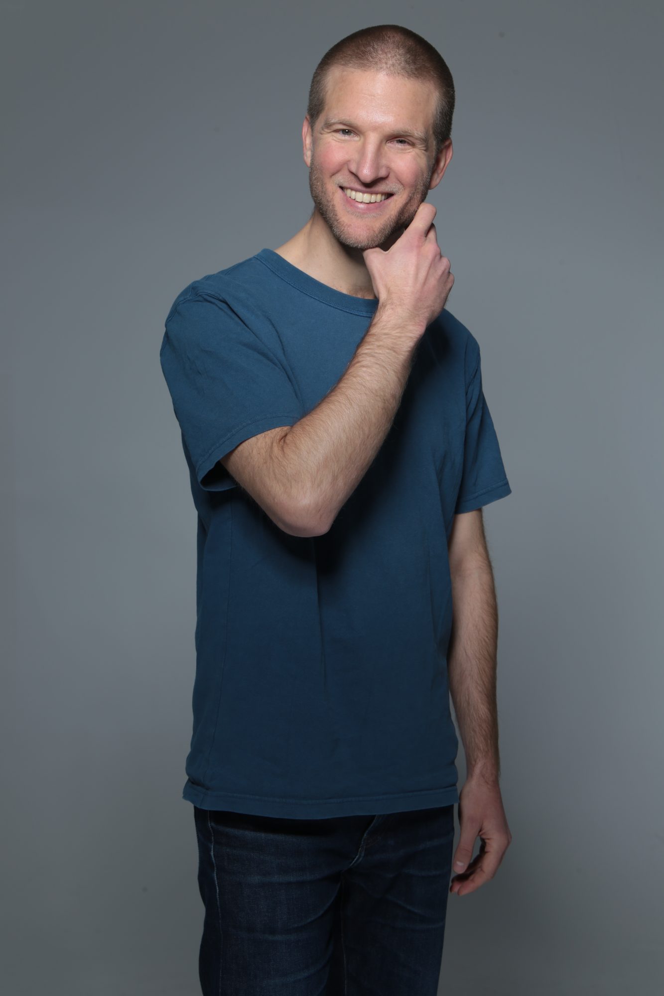 Portrait studio, main au menton, t-shirt bleu, fond gris