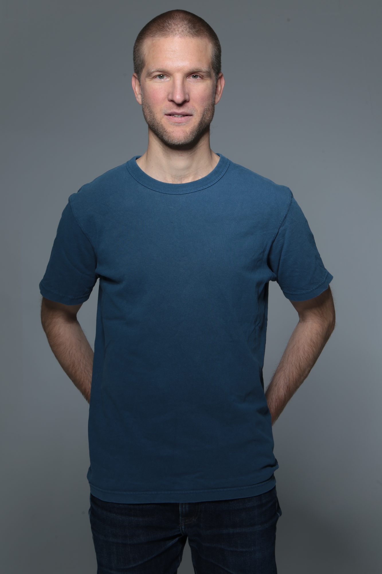 En buste, mains sur les hanches, t-shirt bleu, fond gris