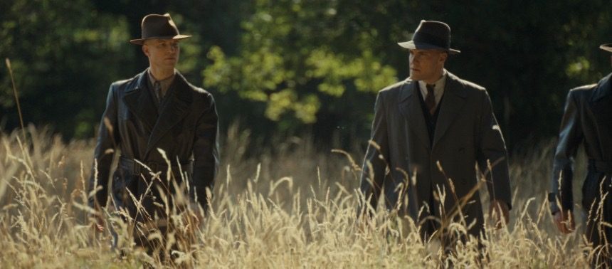 Plan large : deux hommes en manteau et chapeau marchent dans les hautes herbes